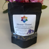 Black package of House Tisane Violet Fairy Herbal Fruit Tea with a colorful label against a floral background.